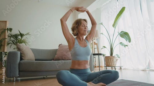 Cinematic storytelling video of a senior old woman practicing yoga and stretching fitness at home. Representation of healthy lifestyle and leisure activities during seniority and the third age