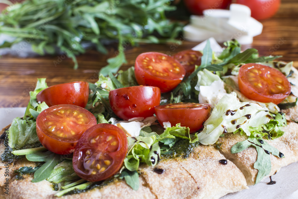 Homemade pinsa with cheese, tomatoes, cabbage and arugula close-up sharpness in the foreground. Homemade pinsa with cheese, tomatoes, cabbage and arugula close-up sharpness in the foreground.
