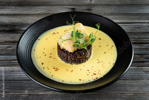 Risotto with slice roasted white fish, cod on black background. Grilled code with mix brown and wild rice in dark style.