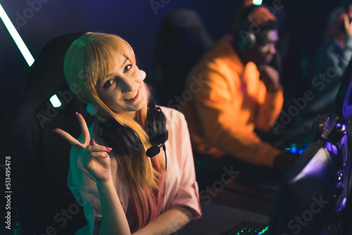 Cyber space concept. Young caucasian beautiful gamer girl with long, blond hair, showing v-sign to the camera, and smiling. PC bang. High quality photo