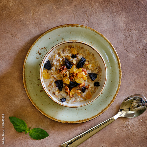 Buckwheat porridge with walnut, raisins and prunes on a green plate on a brown background under concrete.