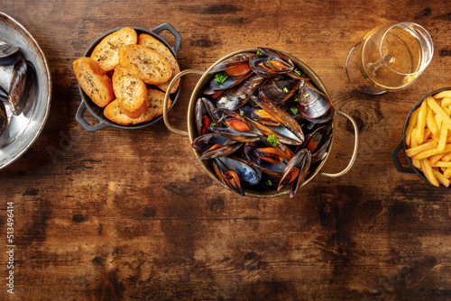 Cooked mussels with toasted bread and white wine, shot from the top on a dark rustic wooden background with copy space