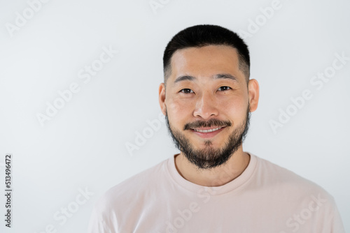 portrait of asian man with beard smiling and looking at camera isolated on grey.