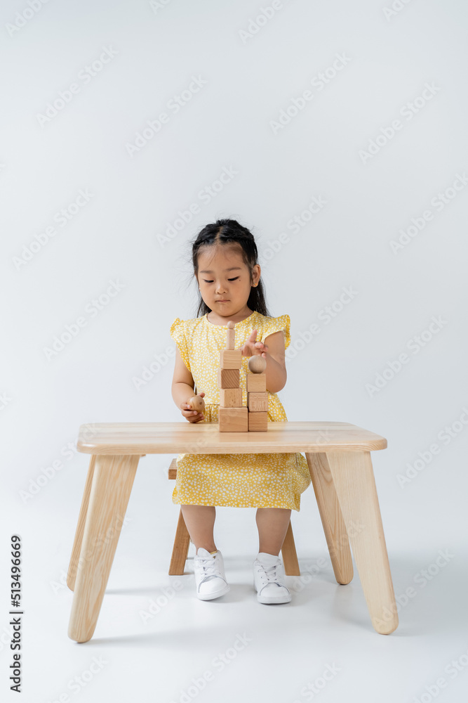 asian preschooler girl in yellow dress playing with wooden shapes on grey. asian preschooler girl in yellow dress playing with wooden shapes on grey.