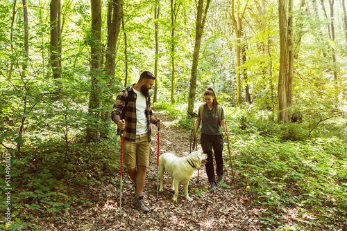 Young happy couple and their dog at hiking through the woods enjoying the sight. Two nature lovers in the mountain forest enjoy healthy walking through the nature. With film grain