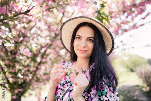 woman with dark hair in a straw hat near cherry blossoms in spring