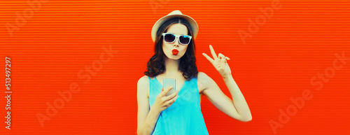 Portrait of caucasian young woman with smartphone wearing summer straw hat on red background