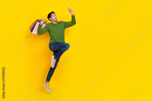 Photo of funky funny guy dressed green pullover jumping holding bags portrait device empty space isolated yellow color background