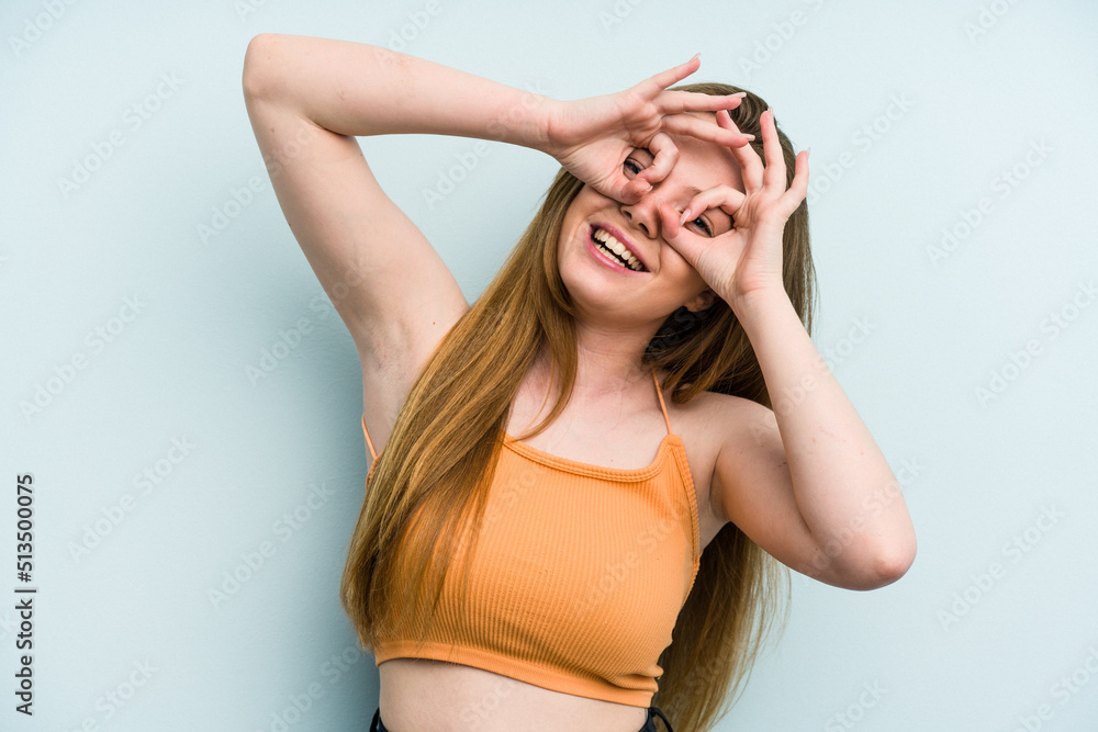 Young caucasian woman isolated on blue background showing okay sign over eyes