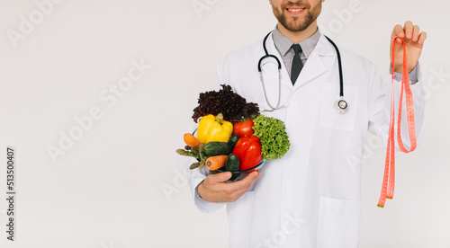 The male doctor nutritionist with stethoscope holding fresh vegetables and ruler on white background photo
