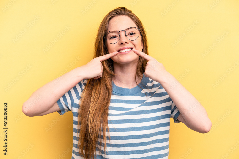 Young caucasian woman isolated on yellow background smiles, pointing fingers at mouth. Young caucasian woman isolated on yellow background smiles, pointing fingers at mouth.