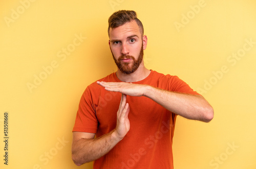 Young caucasian man isolated on yellow background showing a timeout gesture.