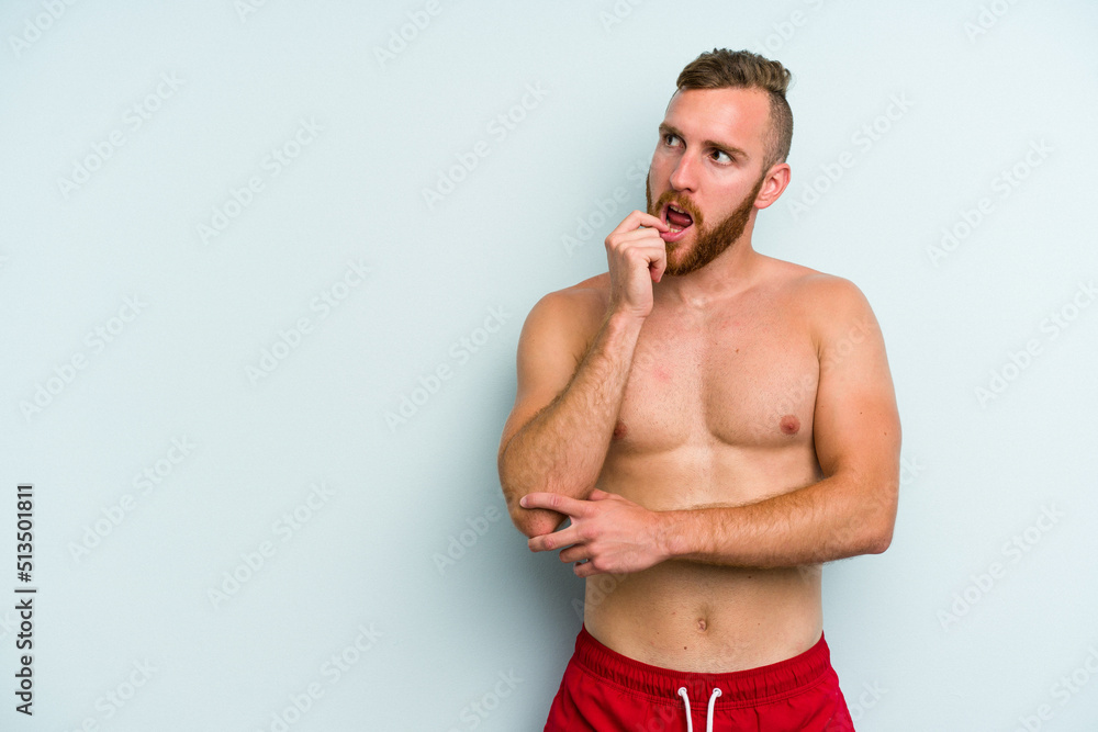 Young caucasian man wearing a swimsuit isolated on blue background relaxed thinking about something looking at a copy space. Young caucasian man wearing a swimsuit isolated on blue background relaxed thinking about something looking at a copy space.