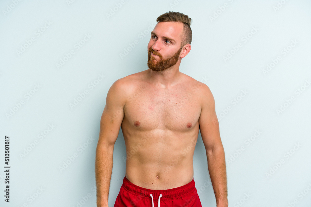 Young caucasian man wearing a swimsuit isolated on blue background confused, feels doubtful and unsure.