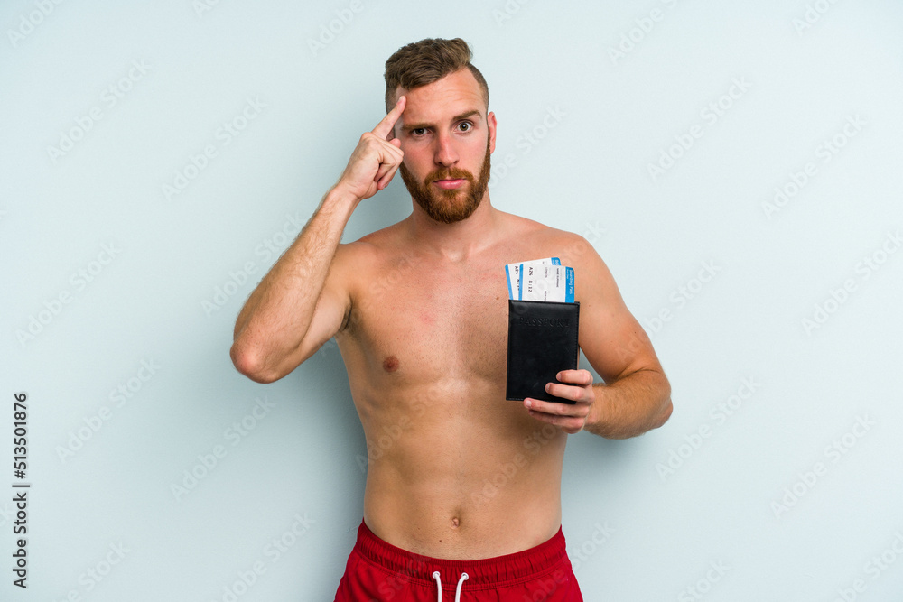Fototapeta premium Young caucasian man holding a passport isolated on blue background pointing temple with finger, thinking, focused on a task.