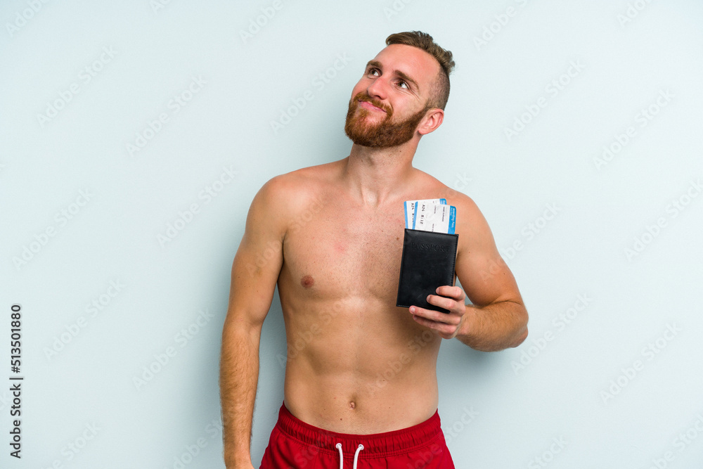 Young caucasian man holding a passport isolated on blue background dreaming of achieving goals and purposes Young caucasian man holding a passport isolated on blue background dreaming of achieving goals and purposes