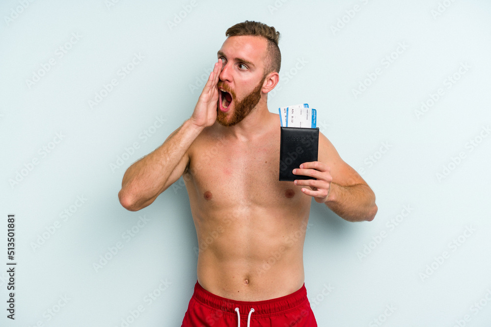 Young caucasian man holding a passport isolated on blue background shouting and holding palm near opened mouth. Young caucasian man holding a passport isolated on blue background shouting and holding palm near opened mouth.