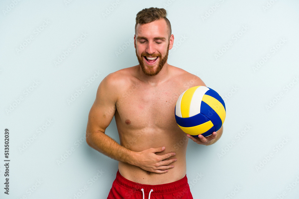 Young caucasian man playing volleyball isolated on blue background laughing and having fun.