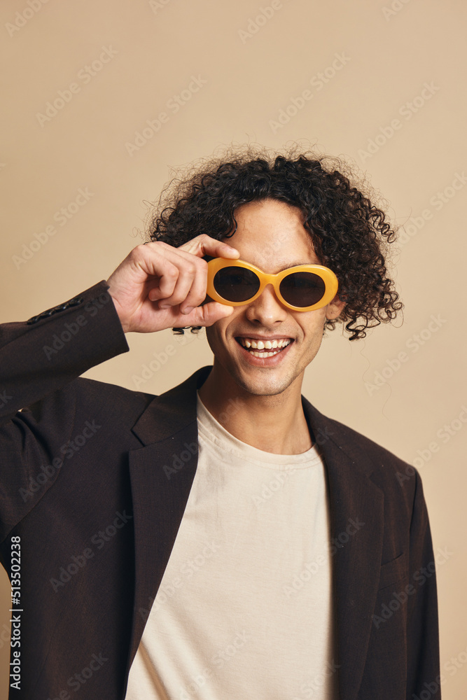 Defiant awesome tanned curly man in classic brown jacket trendy sunglasses posing isolated on over beige pastel background. Fashion New Collection offer. Retro style concept. Free place for ad Defiant awesome tanned curly man in classic brown jacket trendy sunglasses posing isolated on over beige pastel background. Fashion New Collection offer. Retro style concept. Free place for ad
