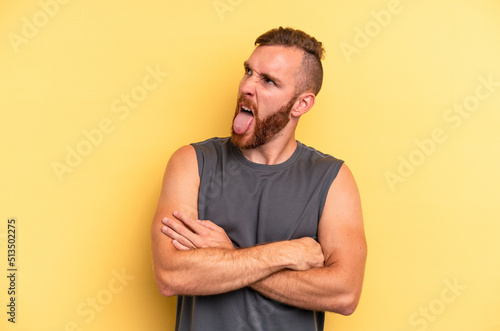 Young caucasian man isolated on yellow background funny and friendly sticking out tongue. © Asier