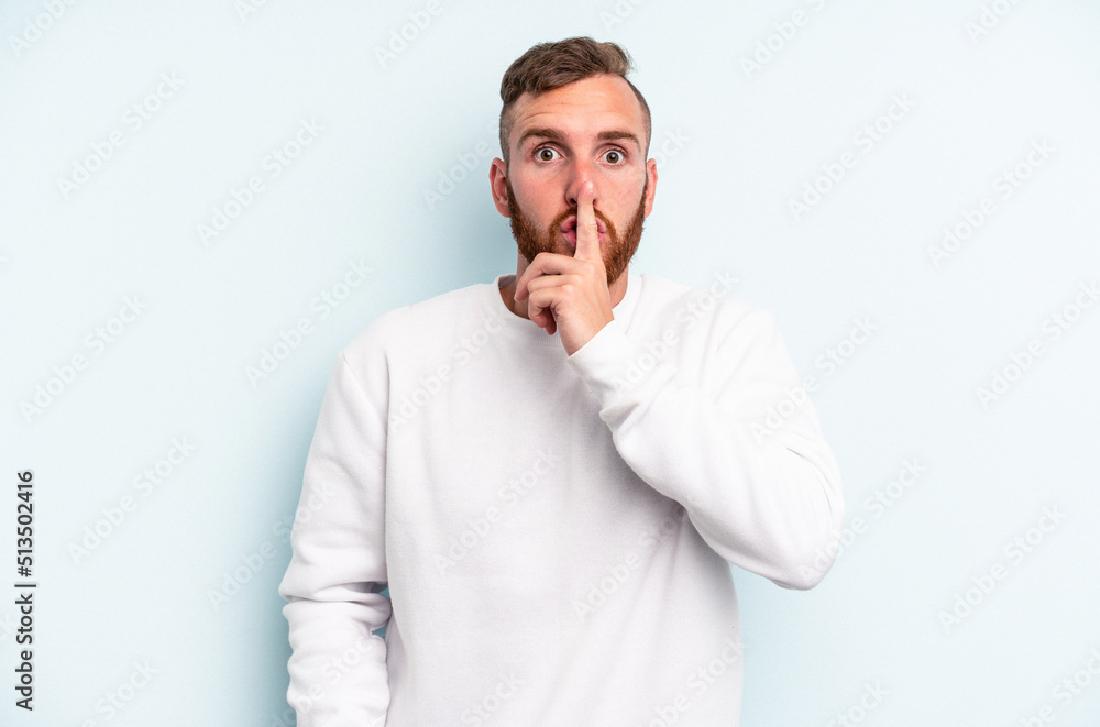 Young caucasian man isolated on blue background keeping a secret or asking for silence.