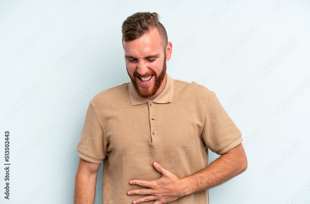 Obraz premium Young caucasian man isolated on blue background touches tummy, smiles gently, eating and satisfaction concept.