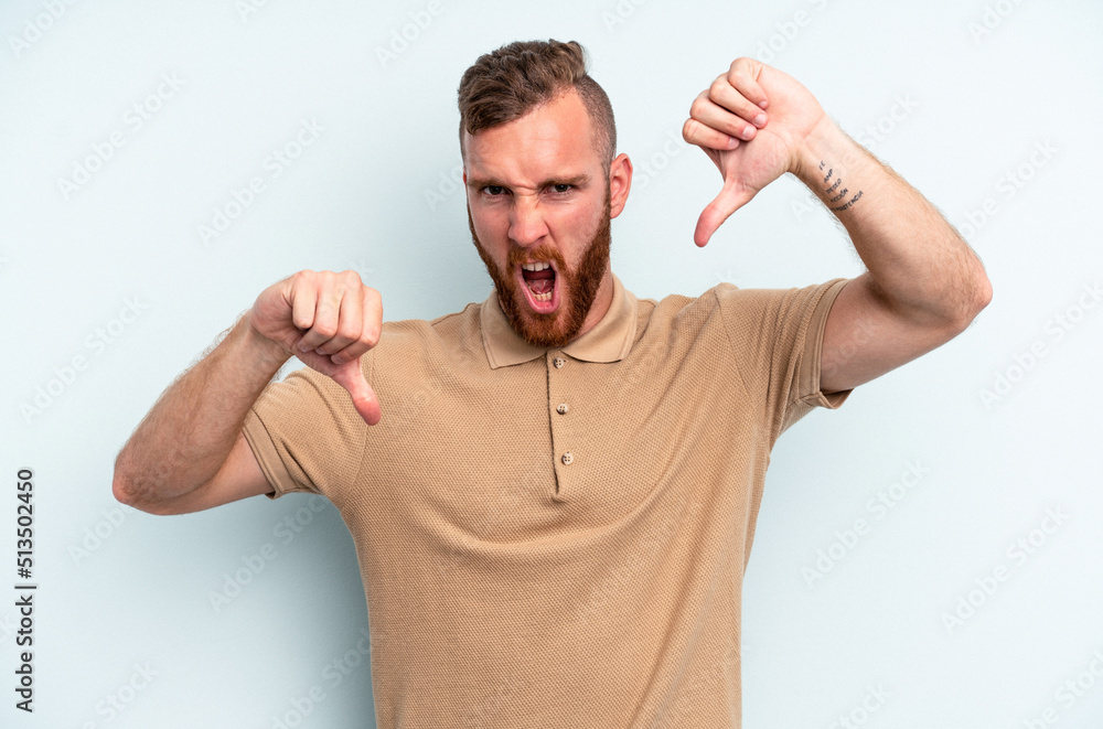 Young caucasian man isolated on blue background showing thumb down and expressing dislike. Young caucasian man isolated on blue background showing thumb down and expressing dislike.