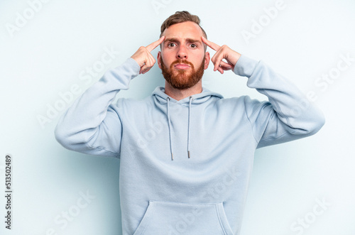 Young caucasian man isolated on blue background focused on a task, keeping forefingers pointing head. © Asier