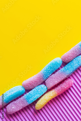 Flat lay of colorful gummy sweets on pink and yellow background.