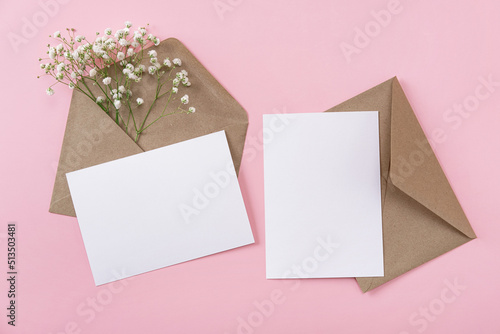Blank greeting cards and envelopes with gypsophila on pink background. Blank paper sheet cards with mockup copy space. Minimal workplace composition. Flat lay, top view
