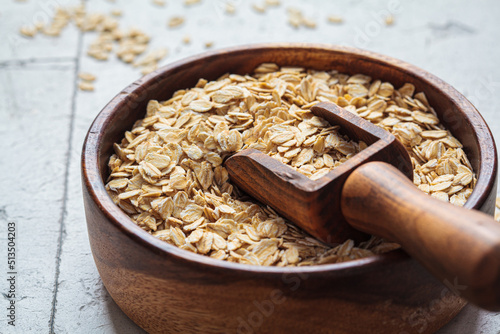 Raw dry oatmeal in wooden bowl, gray background.