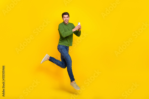 Photo of attractive impressed guy dressed green pullover jumping reading modern gadget empty space isolated yellow color background