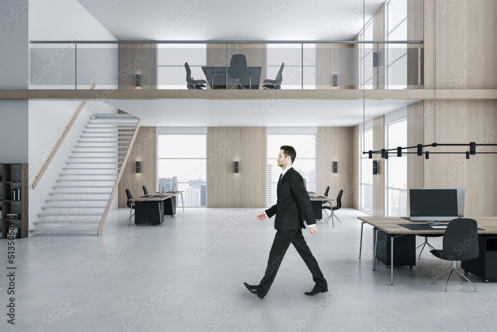 Fototapeta premium Young businessman walking in modern two floors wooden and concrete duplex office interior with panoramic city view, furniture and daylight. Worker and ceo concept.