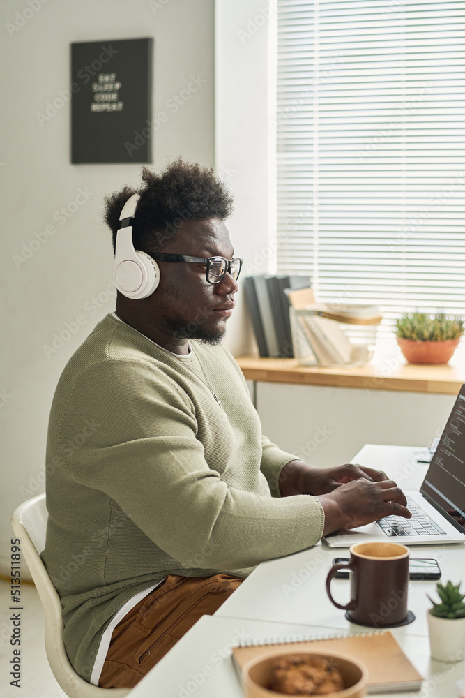 Fototapeta premium African young software developer in wireless headphones concentrating on his online work on laptop