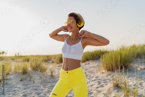 happy smiling woman listening to music in colorful yellow headphones on sunny beach in summer
