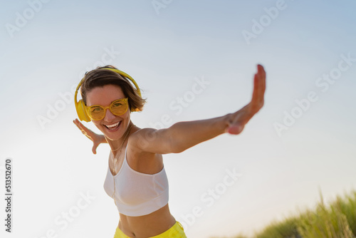 happy smiling woman listening to music in colorful yellow headphones on sunny beach in summer © mary_markevich