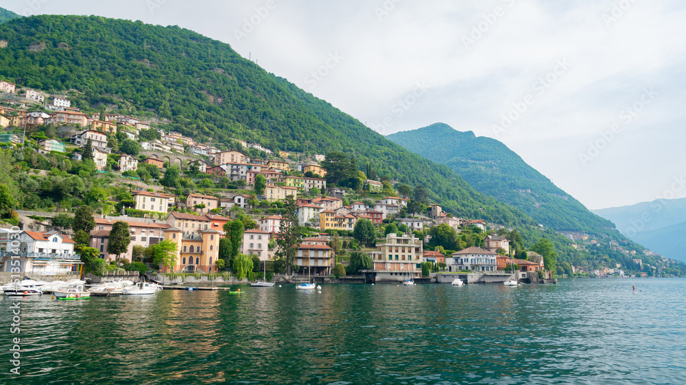 The coastline of the famous Lake Como, Lombardy, Italy, with one of its beautiful villages. Green hills and mountains on the background.