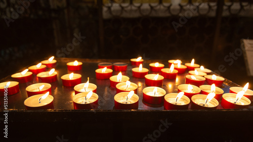 Fotografia Perspective of a multitude of burning candles with flames in a italian cathedral, posed by believers after a prayer