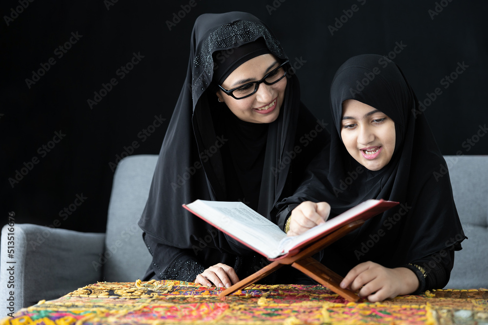 muslim mother with her daughter reading a holy book or Quran on sofa and black background muslim mother with her daughter reading a holy book or Quran on sofa and black background