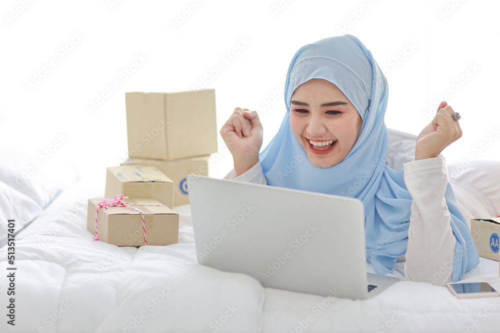 Beautiful and young asian woman in muslim sleepwear with attractive look, lies on bed with computer, mobile phone and online package box delivery. Smart girl with hijab receive good news and surprise. Beautiful and young asian woman in muslim sleepwear with attractive look, lies on bed with computer, mobile phone and online package box delivery. Smart girl with hijab receive good news and surprise.