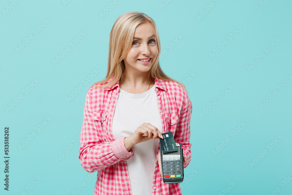 Young happy smiling woman she 30s in pink shirt white t-shirt hold wireless modern bank payment terminal to process acquire credit card payments isolated on plain pastel light blue background studio. Young happy smiling woman she 30s in pink shirt white t-shirt hold wireless modern bank payment terminal to process acquire credit card payments isolated on plain pastel light blue background studio.