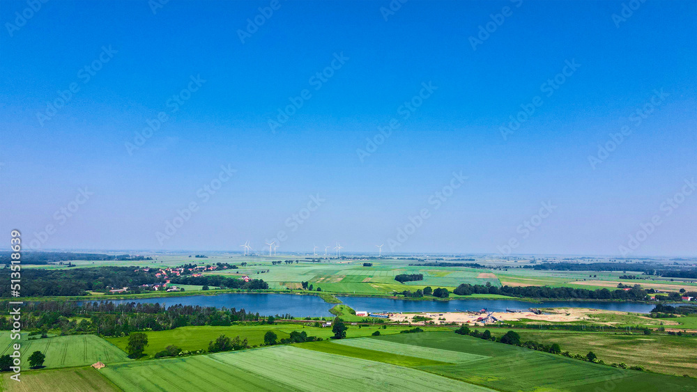 Windmill turbine generator against blue sky in countryside with green fields and lake, Concept of clean, renewable, sustainable, alternative energy