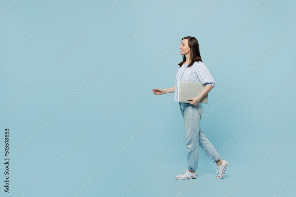Full body side view young happy smiling woman she 20s wear casual blouse hold closed laptop pc computer walk go hurry up isolated on pastel plain light blue background studio People lifestyle concept Full body side view young happy smiling woman she 20s wear casual blouse hold closed laptop pc computer walk go hurry up isolated on pastel plain light blue background studio People lifestyle concept