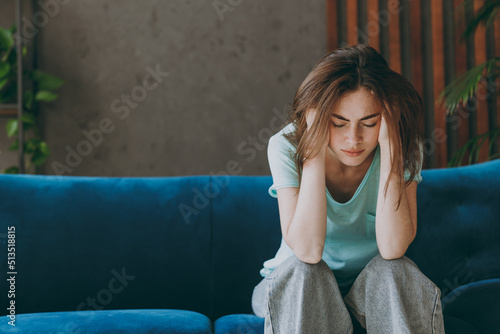 Canvas Print Young frustrated ill woman she 20s wear casual clothes mint t-shirt holding head suffer from headache close eyes sit on blue sofa indoor rest at home in own room apartment