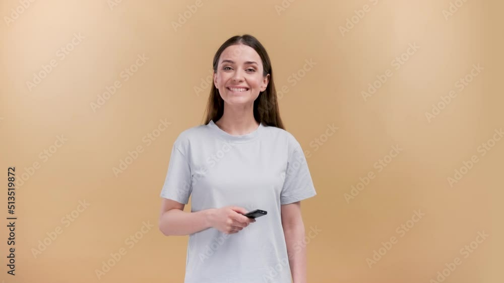 Attractive cheerful girl switching channel having fun with a delighted smile isolated over beige pastel color background Attractive cheerful girl switching channel having fun with a delighted smile isolated over beige pastel color background