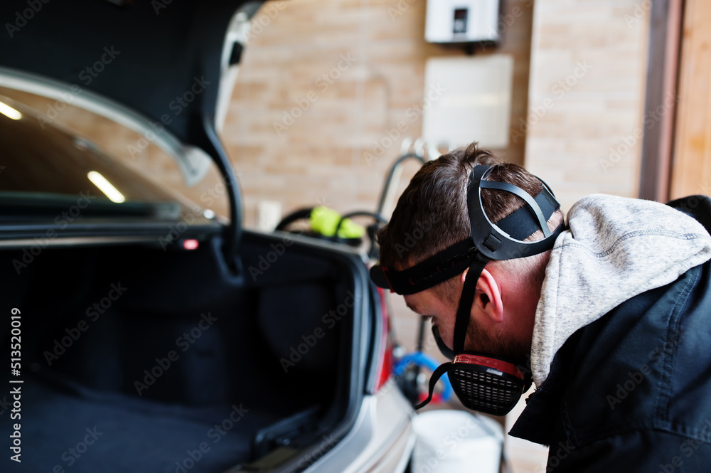 Man in uniform and respirator, worker of car wash center, cleaning car interior with hot steam cleaner. Car detailing concept.