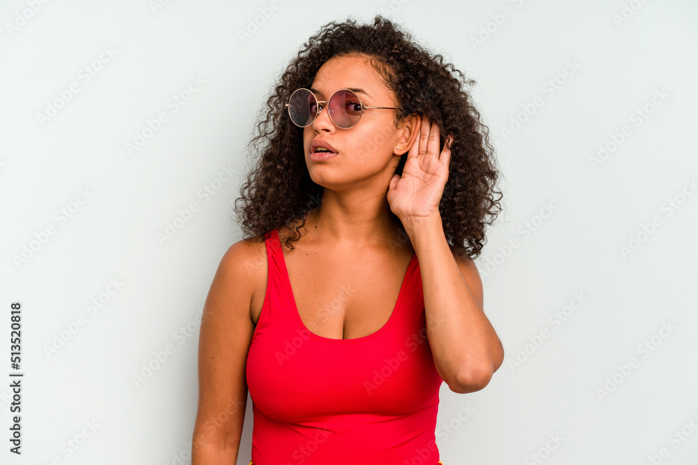 Young brazilian woman wearing a swimsuit isolated on blue background trying to listening a gossip. Young brazilian woman wearing a swimsuit isolated on blue background trying to listening a gossip.