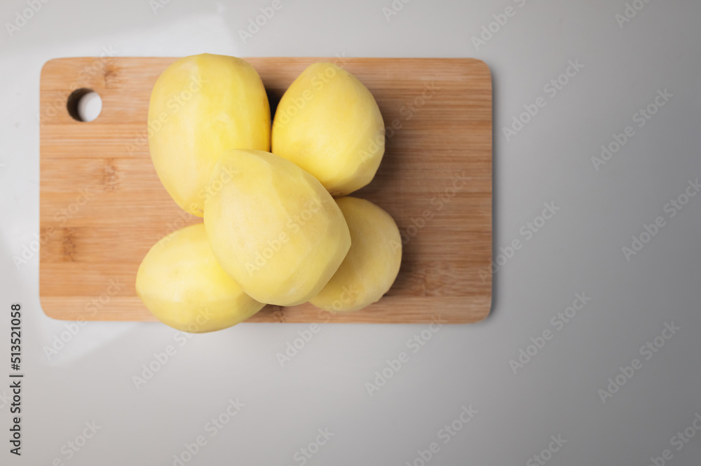 Peeled fresh potatoes lie on a wooden cutting board on a white table