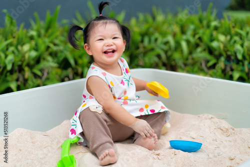 Asian baby laugh and play sand in sandbox at outdoor. 1 year 6 month baby enjoy to play sand use as concept of play, health, mood and motion of baby and kid development.