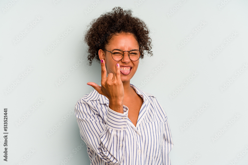 Young Brazilian woman isolated on blue background showing rock gesture with fingers Young Brazilian woman isolated on blue background showing rock gesture with fingers